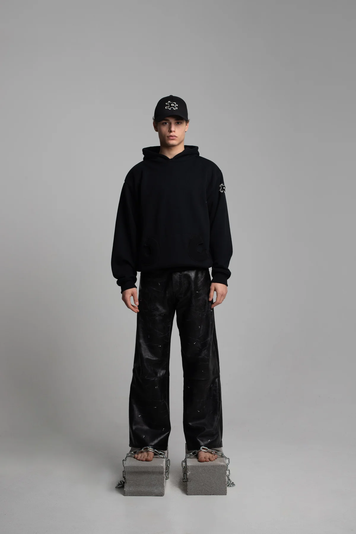 Model in a black COLLAPSE hoodie and trousers on concrete blocks