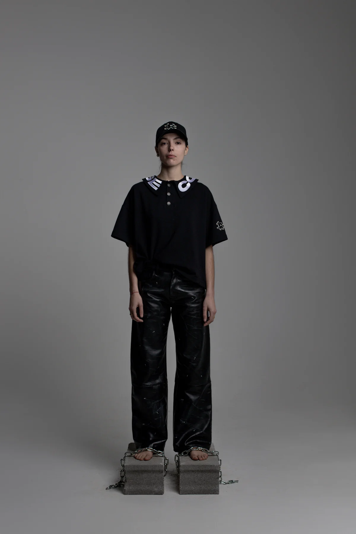 Black COLLAPSE polo look with cap on concrete blocks
