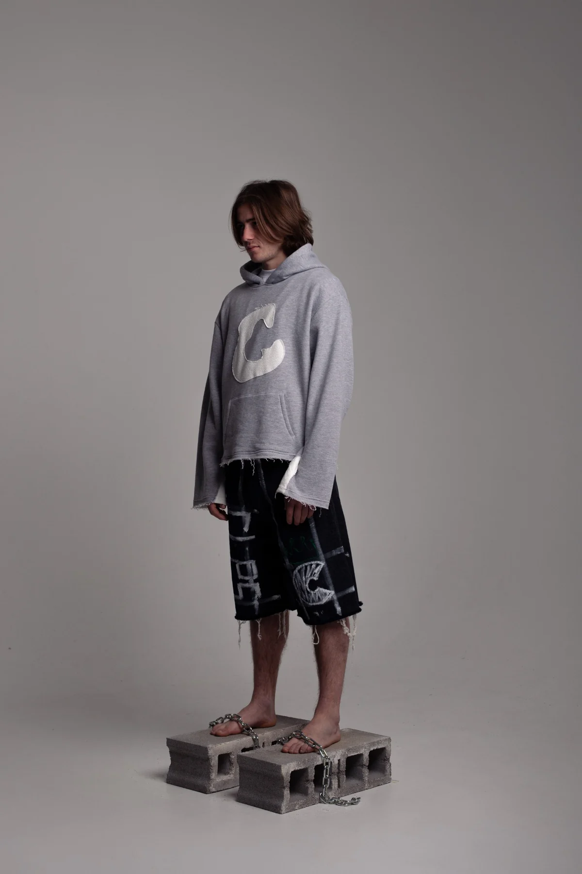 Man wearing the same grey C Logo hoodie and the same graphic COLLAPSE shorts